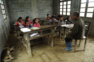  李光友在给学生上课。一只狗悠闲地逛进教室，伴随着朗朗的读书声席地而睡。