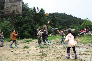  教室前面的泥地里，竖起篮球架，就是篮球场。雨季来了，孩子们穿着水鞋上学。