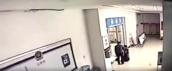 该男子跪在办证厅门口，一旁有交警队工作人员在劝说。来源：视频截图