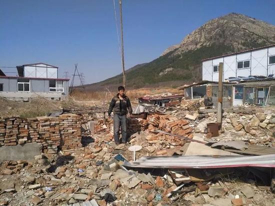  裘国金站在变成一片废墟的家中