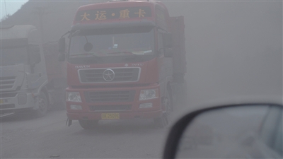 信发铝厂厂区外道路上，大货车来往不断，扬起粉尘。