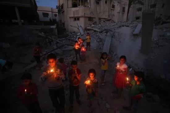 5月7日，巴勒斯坦儿童在加沙南部拉法地区一遭以色列空袭的房屋废墟上手握蜡烛祈祷。新华社发（哈立德&middot;奥马尔摄）