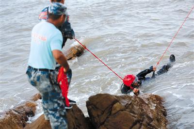 搜救中，队员们紧紧地拉着保护绳，以防潜水员被浪拍到礁石上受伤。