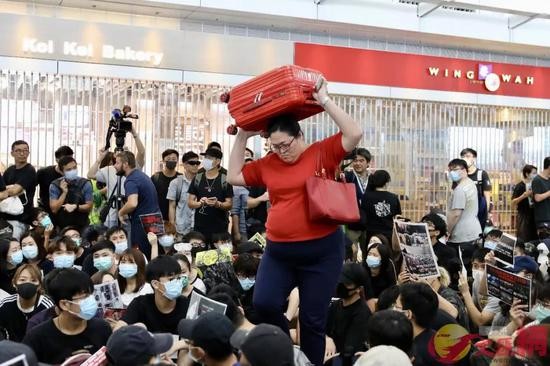 正扛着行李箱穿过非法示威者的女士，以及身后落闸停业的商铺