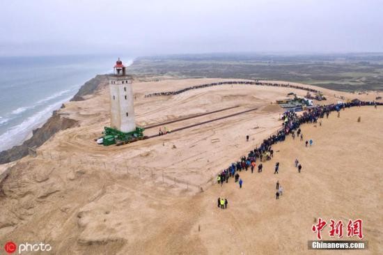 当地时间10月22日,丹麦日德兰半岛,丹麦Rubjerg Knude灯塔将进行迁移。该灯塔约有120年历史,1900年首次亮起,曾经位于距离海岸线200米处,由于海岸被侵蚀和流沙问题,现在距离海岸仅有6米,不得不迁移。由于流沙的不断堆积和海岸的持续侵蚀,这座独具魅力的历史性灯塔于1968年被迫废弃。图为工人们将灯塔架在车轮和铁轨上,试图将其向北移动80米。图片来源:ICphoto