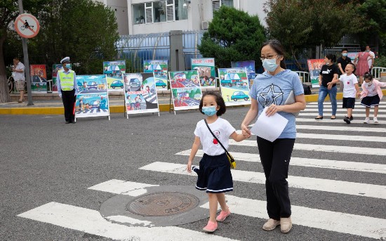 上地实验学校路口,家长带着孩子过马路,送他们上学,交通协管员在路旁站岗维持秩序。摄影/新京报记者 李凯祥