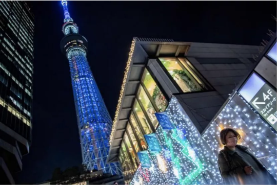 12月23日,一名戴口罩的女子走在点缀着圣诞灯饰的日本东京街头