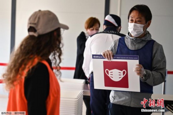 资料图:2020年10月21日,东京奥运会和残奥会组织委员会21日在东京向媒体公开了,观众等进入赛场时通过的行李安检区运营的实证试验。图为志愿者提示被检测者注意佩戴口罩。