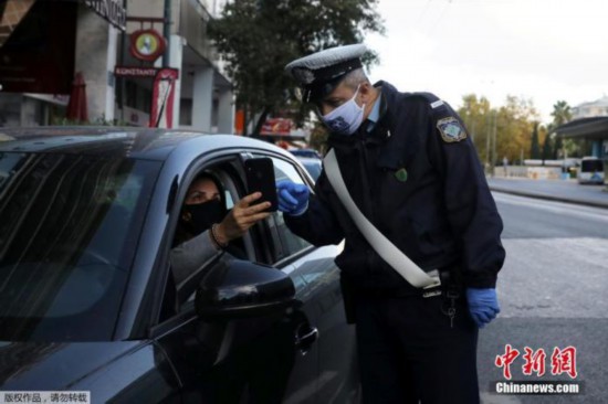 当地时间11月7日，希腊雅典，一名警察正在检查司机证件，确定其出行目的。为遏制新冠疫情，自当地时间7日早晨6时起，希腊全国进入为期三周的封锁状态。新的限制措施将禁止区域间的旅行。