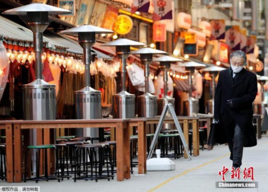 资料图：当地时间1月7日，日本东京，一名路人路过空荡的户外餐馆。