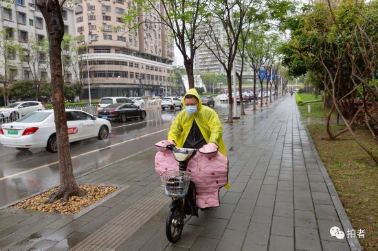 △ 2021年4月3日，路上车水马龙，一名路人穿着雨衣防雨。