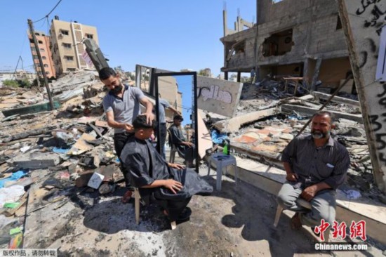 当地时间5月25日,加沙地区,巴勒斯坦理发师Hashim Al-Jarousha在废墟上为民众理发。据悉,他的理发店在巴以冲突中遭以色列空袭被摧毁。