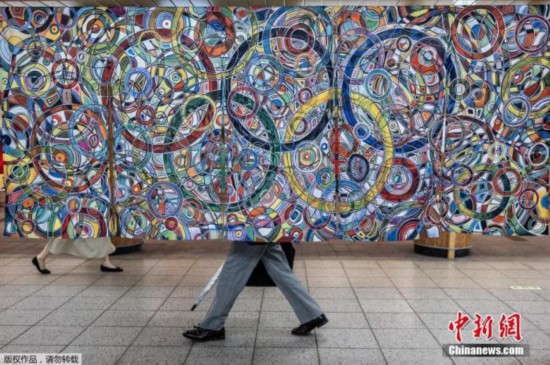 东京街头洋溢奥运气息，图为东京火车站的奥林匹克广场，人们走过前英国奥运标枪运动员罗尔德&middot;布拉德斯托克的画作《奥林匹克之强》。