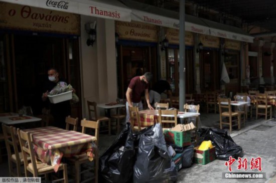 资料图:5月4日消息,希腊餐饮业恢复经营。当地时间5月3日,希腊雅典,一家餐馆的服务生在收拾餐桌。