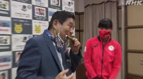 8月4日，日本名古屋市长河村隆之与东京奥运会夺金的日本垒球队代表会面。当选手把金牌戴到河村脖子上时，他突然将金牌放到口中咬了一口，随即遭到民众批评。图片来源：日本放送协会(NHK)视频截图