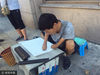 2017年8月24日，山东青岛，在青岛市靠近栈桥附近街头，杨勇宏用仅存的一小部分双臂合拢，将毛笔夹在中央开始挥舞现场写字。