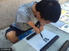 2017年8月24日，山东青岛，在青岛市靠近栈桥附近街头，杨勇宏用仅存的一小部分双臂合拢，将毛笔夹在中央开始挥舞现场写字。