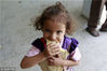 当地时间2015年8月19日，也门萨那，逃离冲突的一名小女孩在临时难民营吃面包。
