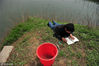 2011年4月10日，在西安长安区杨庄乡的一片鱼塘边，来自韦曲的张先生趴在鱼塘边看书，只等鱼儿投入自己提前在水下设置好的网。