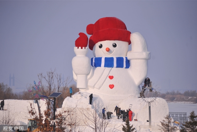 哈尔滨：松花江畔建起近20米高大雪人 头戴红帽手举火炬超治愈