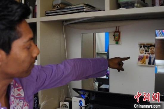 图为一名孟加拉国留学生将自己与妈妈的合影从行李箱取出，贴至墙上。　李娇阳 摄